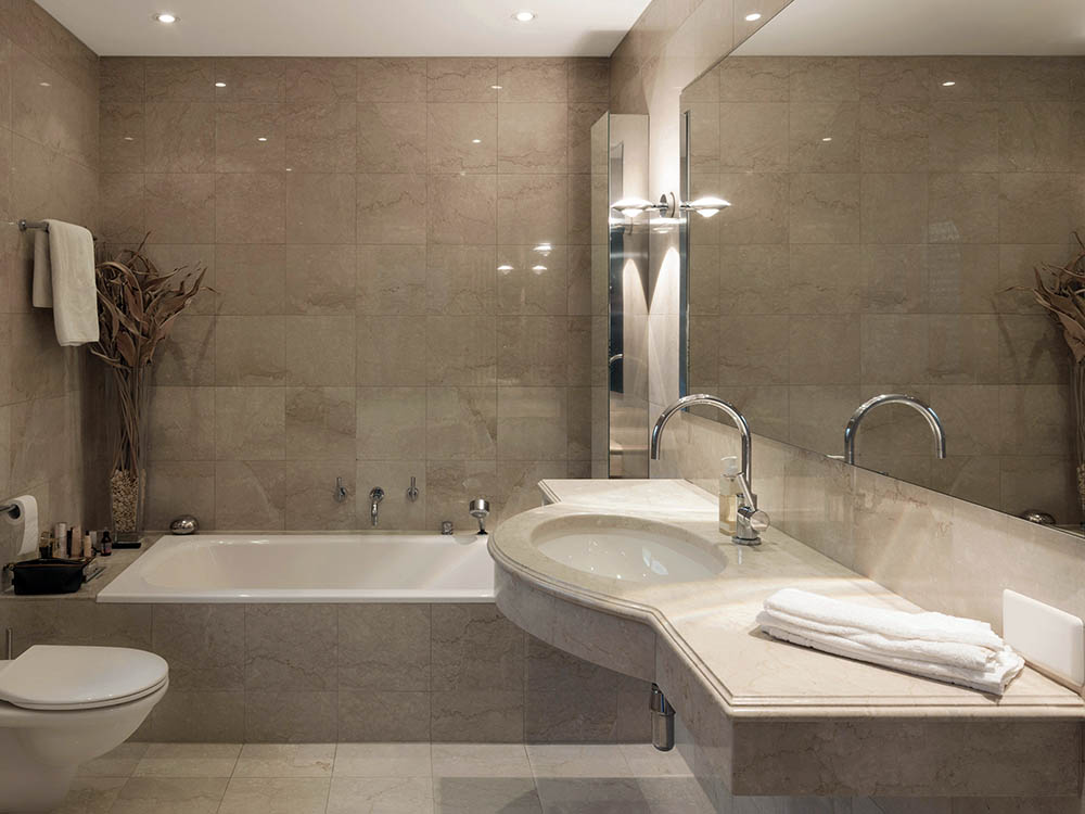 Badezimmer nach der Modernisierung: Naturstein-Optik mit Badewanne und Waschtisch Modernisiertes Luxus-Badezimmer mit großformatigen Fliesen, eleganter Einbaubadewanne und Waschtischplatte – Badsanierung Uwe Kleinheider Hagen a.T.W.